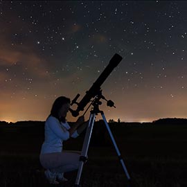 Woman looking through telescope at night sky