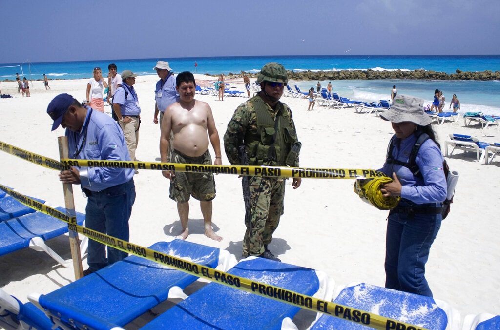 A tourist watches as Mexican federal environmental authorities and navy sailors close a section of beach.