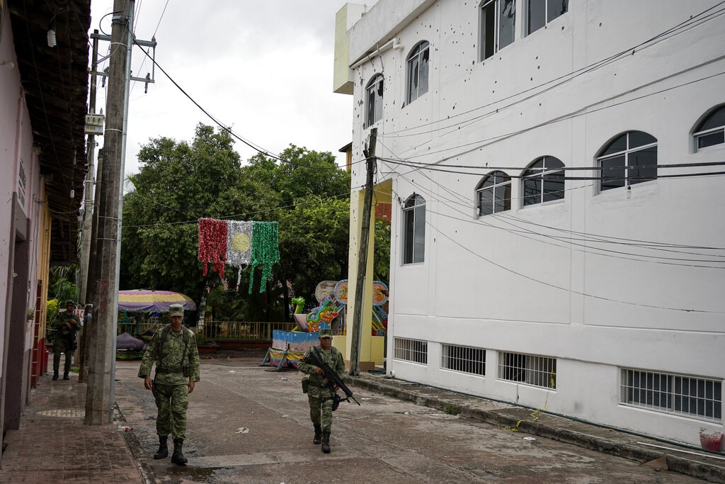 Soldiers walk past the City Hall pocketed with bullet holes the day after a mass shooting in San Miguel Totolapan, Mexico, Thursday, Oct. 6, 2022. 
