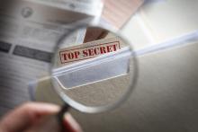 Someone looking at top secret files with magnifying glass