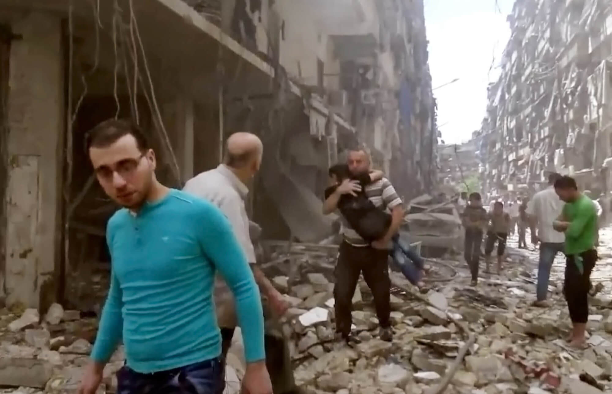 surviors walk through rubble and debris from airstrike in Syria
