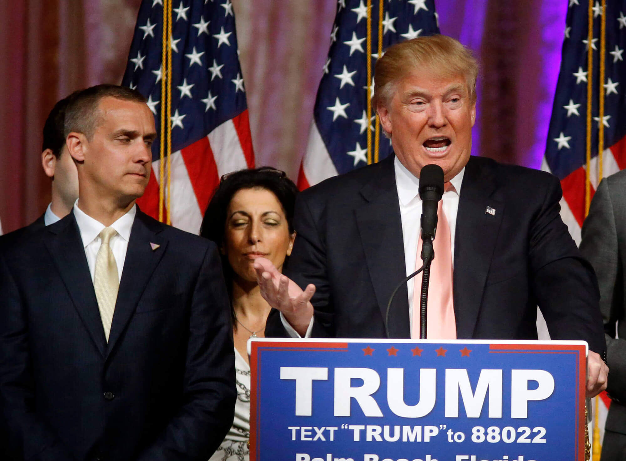 Image of Trump speaking at a campaign event with Corey Lewandowski beside him.