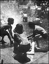 Children Playing in the Cool Stream of an Open Fire Hydrant